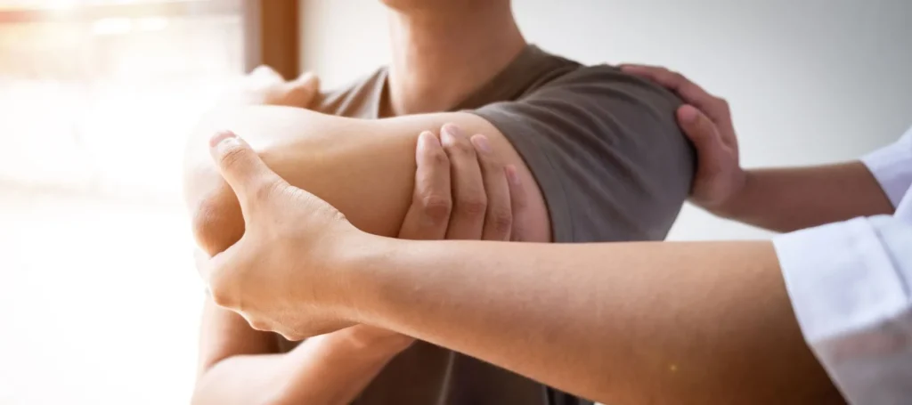 A physical therapist is performing a manual stretch and mobilization on a male patient's shoulder and upper arm.